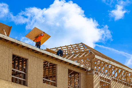Construction workers using fall protection while working on an elevated residential roof under construction.