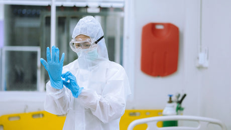 Worker wearing personal protective equipment including safety goggles, protective clothing, face covering, and gloves.